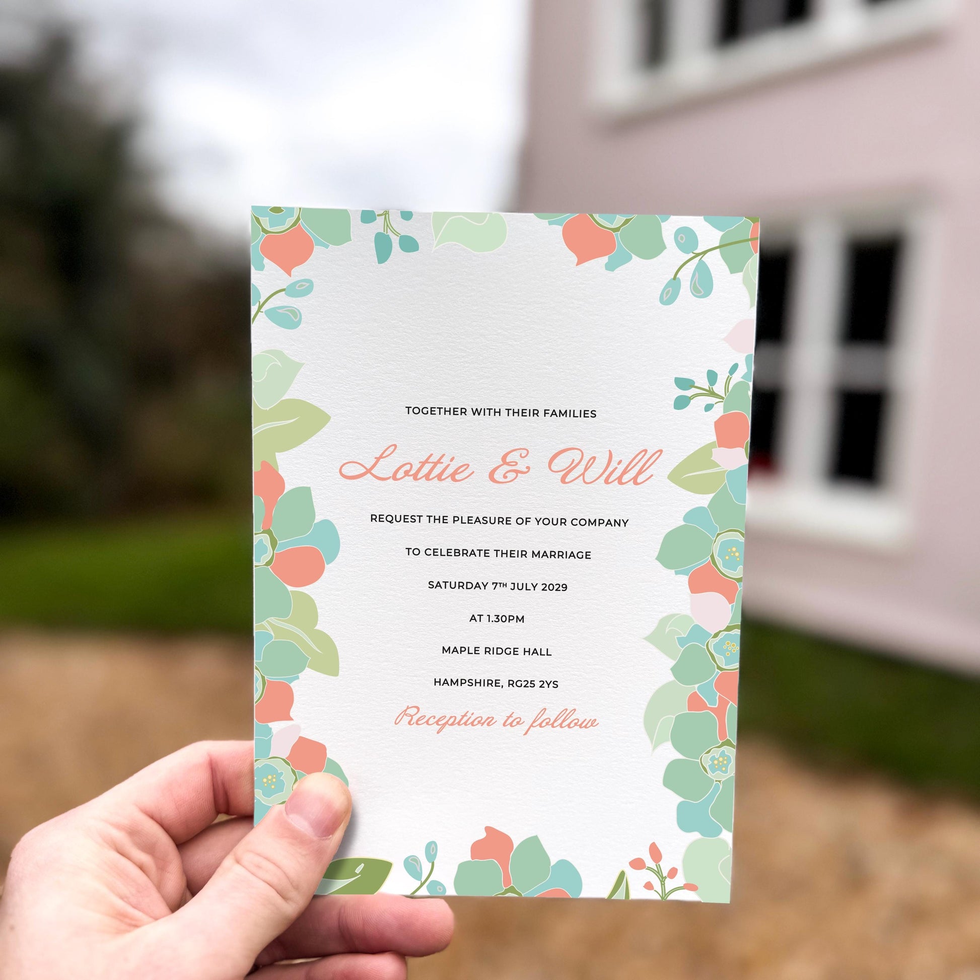 Hand holding a wedding invitation featuring pastel peach, mint and blue retro-style florals framing the design on all sides.