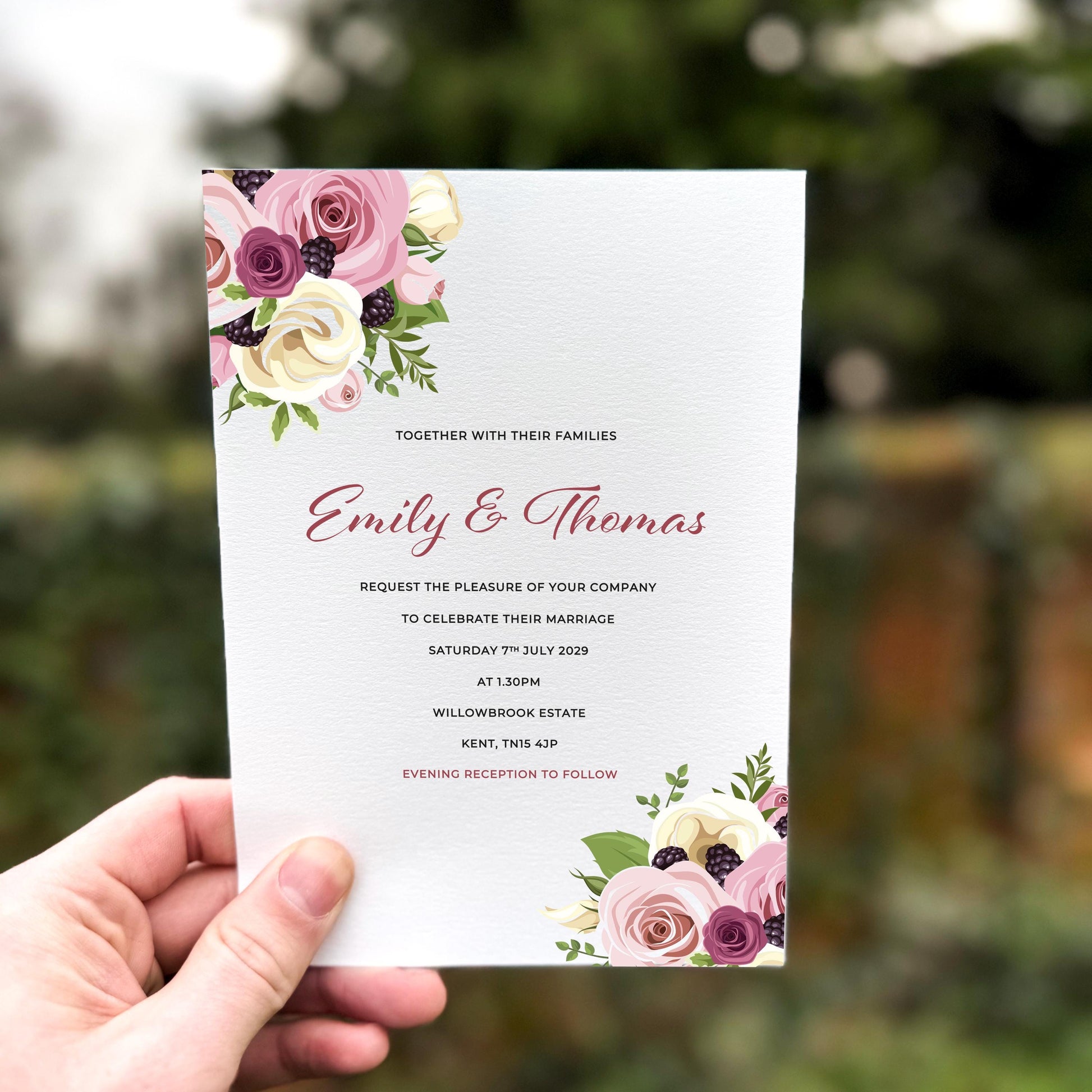 Hand holding a wedding invitation with blush, cream and plum roses paired with berries, printed on textured card with floral clusters at the top left and bottom right.
