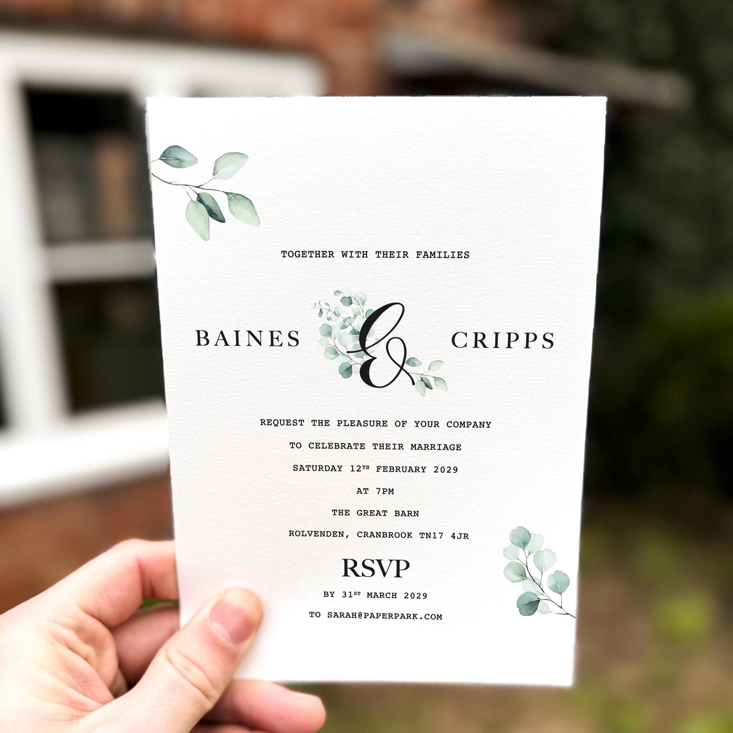 Hand holding a wedding invitation with minimalist eucalyptus leaves printed in soft green tones on textured card.